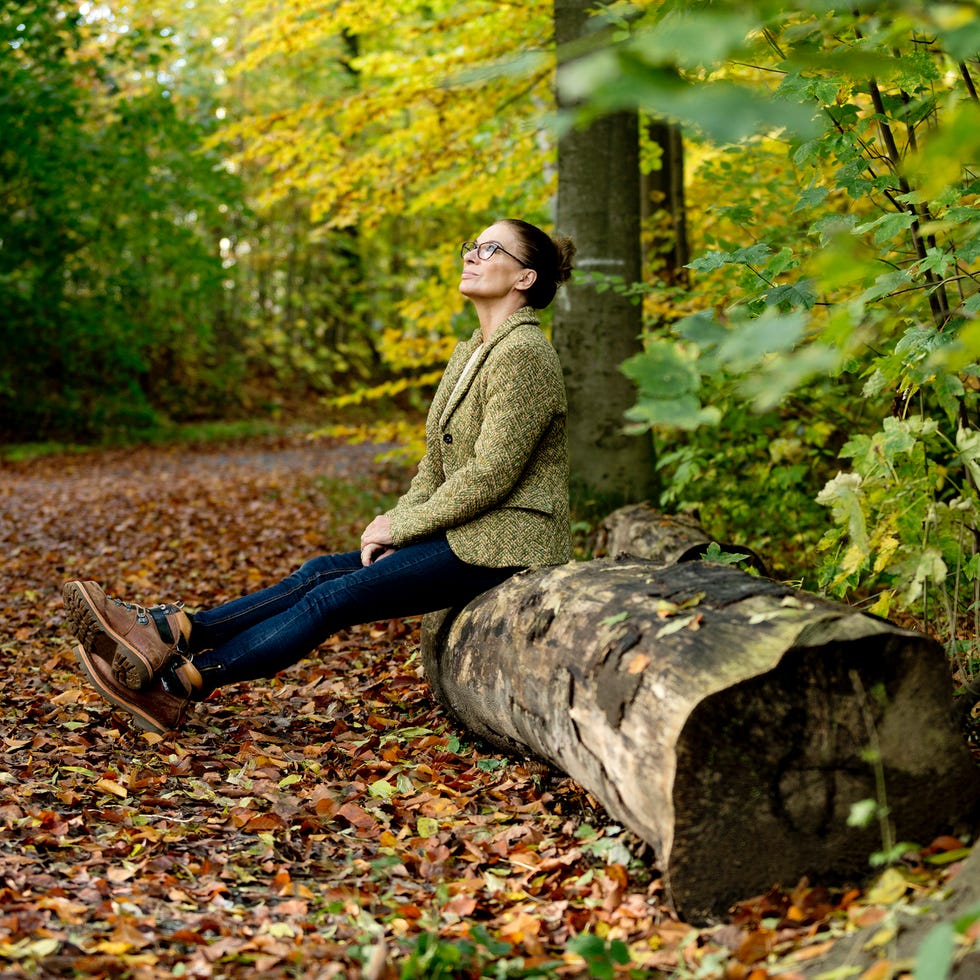 woman sitting on a log in a wooded area with autumn foliage
